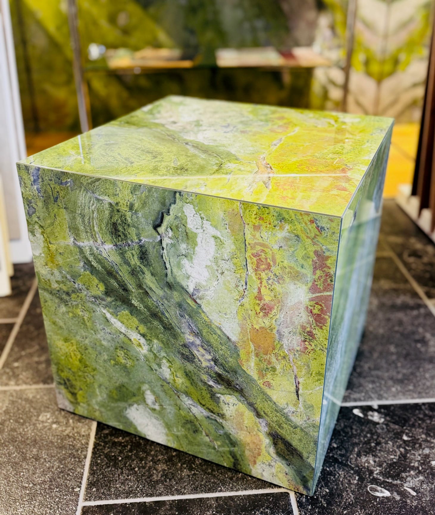 Würfel aus grün geädertem Marmor als Ausstellungsstück auf dunklem Steinboden
