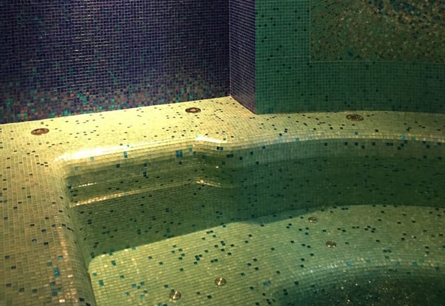 Becken mit grün-goldenem Glasmosaik unter dunkelblauer Wand