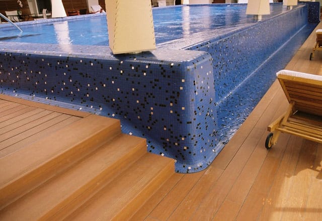Beckenrand aus blauem Mosaik mit dunklen Einlegern, Stufen und Holzdeck