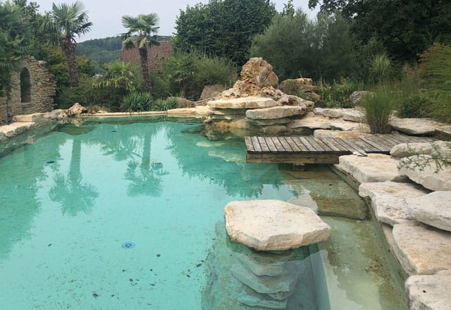 Naturpool mit großen Findlingen, Holzsteg und flachem klarem Wasser