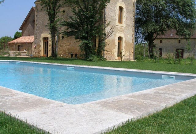 Rechteckiger Pool mit heller Natursteineinfassung vor einem alten Steinhaus