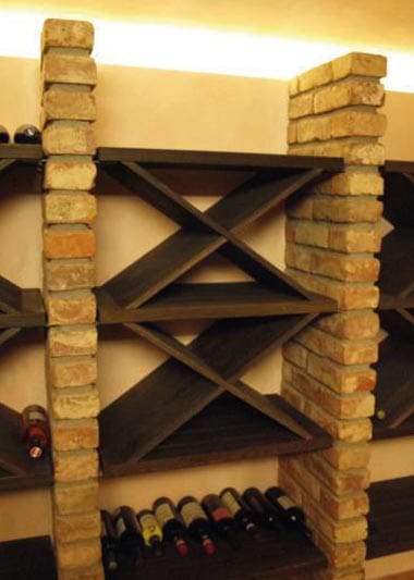 Weinregale in X-Form aus dunklem Holz zwischen gemauerten Ziegelsäulen