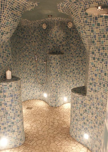 Runde Mosaikdusche mit gemauerten Trennwänden und warmem Licht