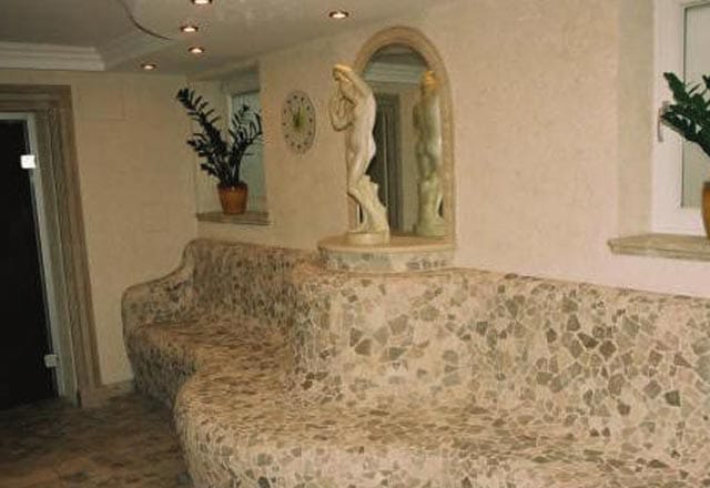 Geschwungene Sitzbank aus Bruchsteinmosaik, dahinter eine Statue in der Wandnische
