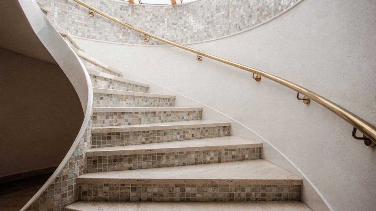 Gewendelte Treppe mit hellen Natursteinstufen, Glasmosaik in den Setzstufen und Messinghandlauf