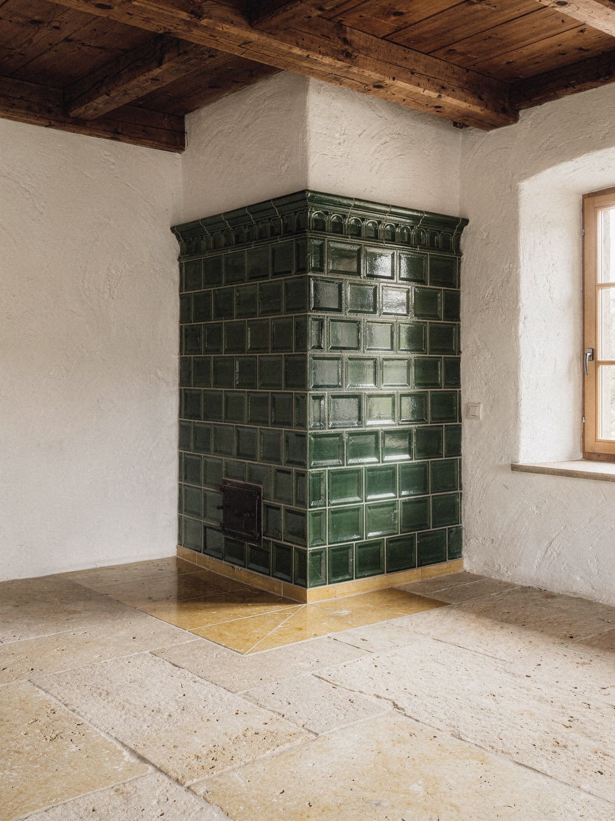 Wohnzimmer eines Landhauses mit grünem Kachelofen, Solnhofner Bodenplatten und Sitzbank am Fenster