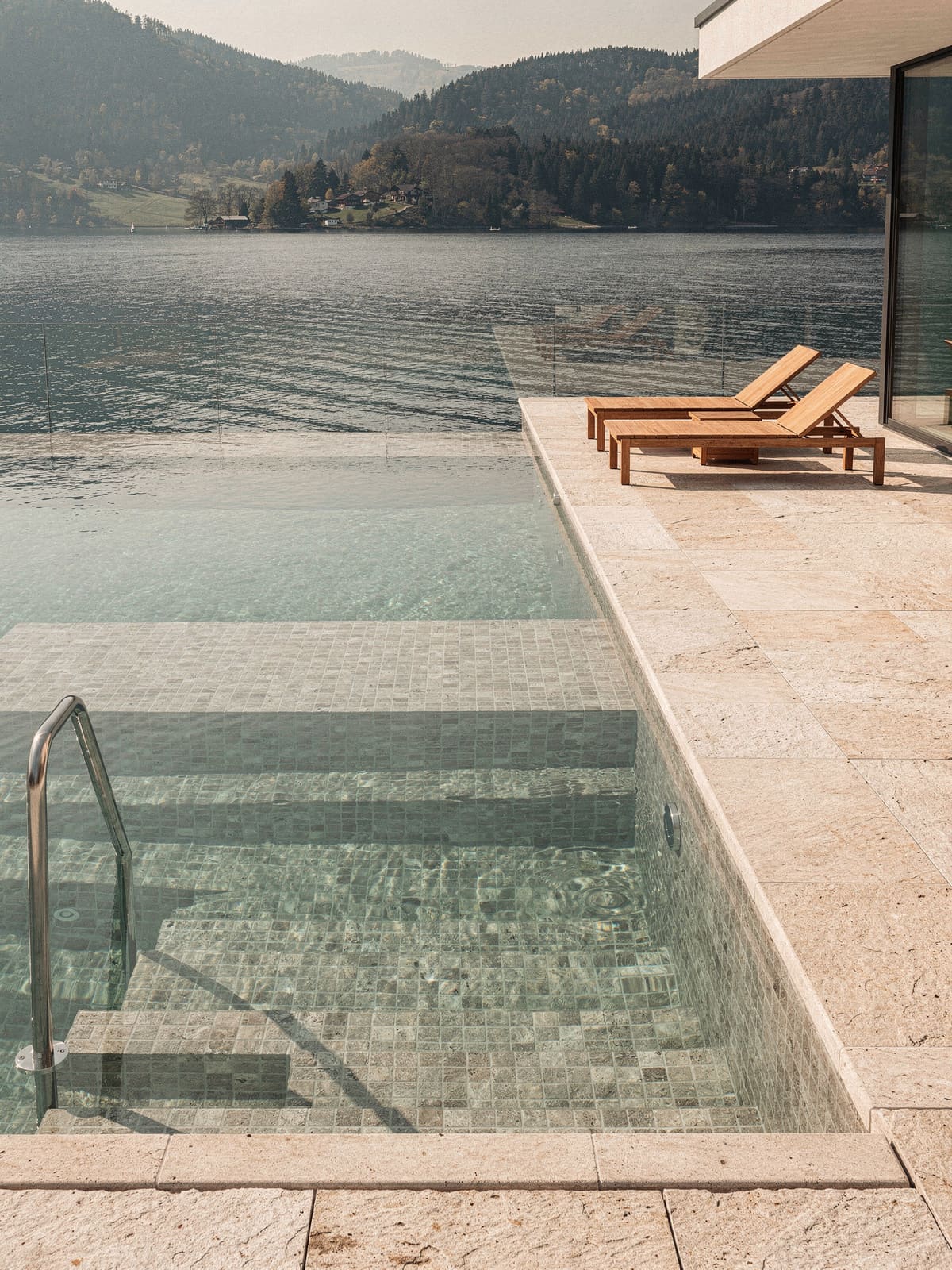 Pool mit Kalkstein-Umrandung und Mosaik im Becken, dahinter der See